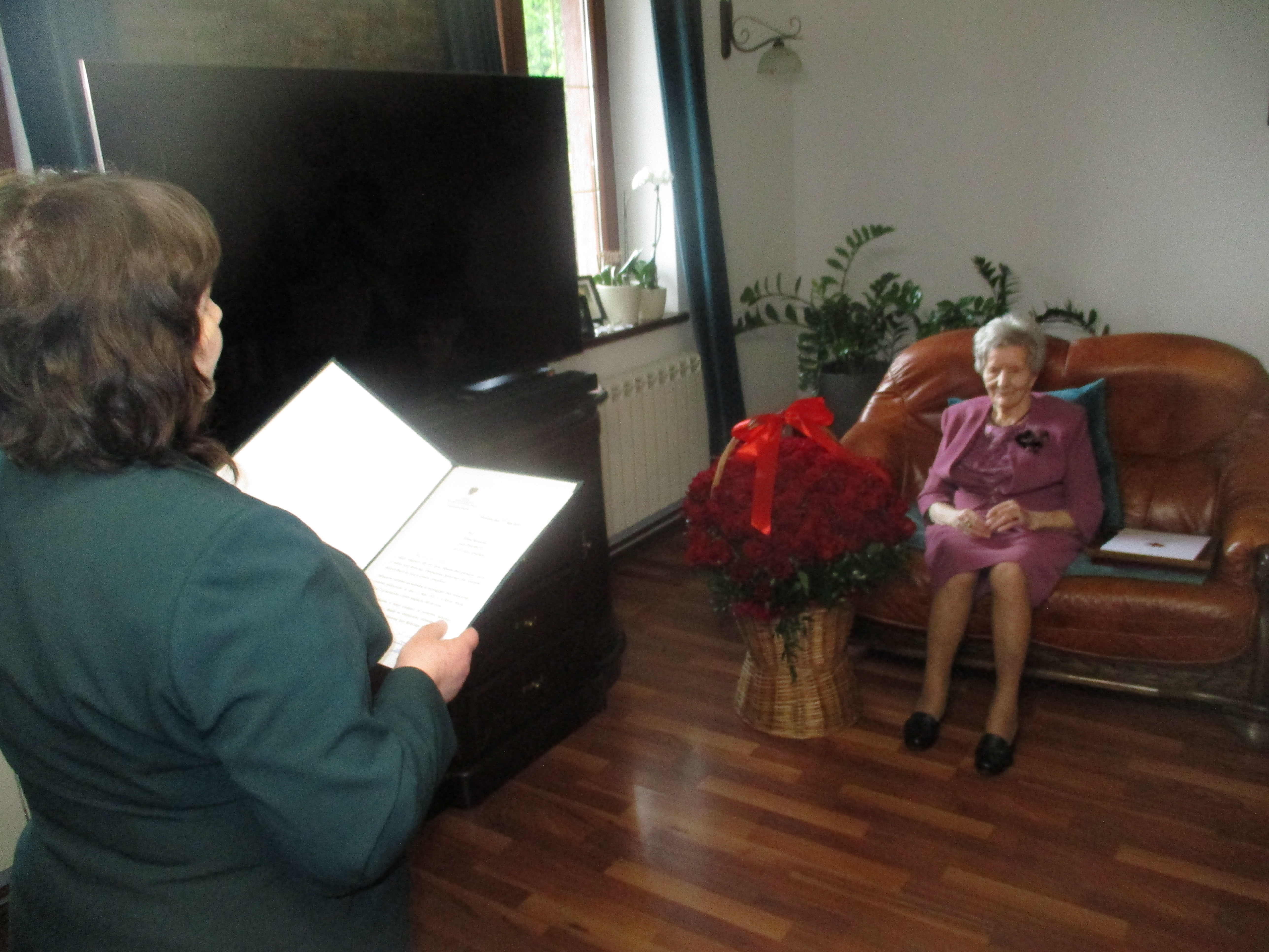 Pani Helena siedzi na kanapie a urzędnik KRUS odczytuje list Prezesa KRUS